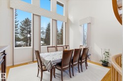 The dining area features high ceilings, hardwood flooring, and an expansive window wall with views of evergreen trees - 