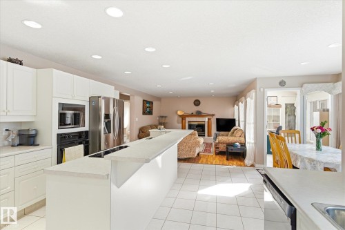 The kitchen features white cabinetry, stainless steel appliances, and a central island with a breakfast bar - 128 Weaver Drive, Edmonton, AB - Indoor Photo Showing Kitchen