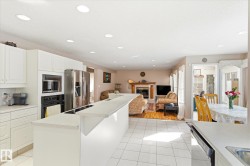 The kitchen features white cabinetry, stainless steel appliances, and a central island with a breakfast bar - 
