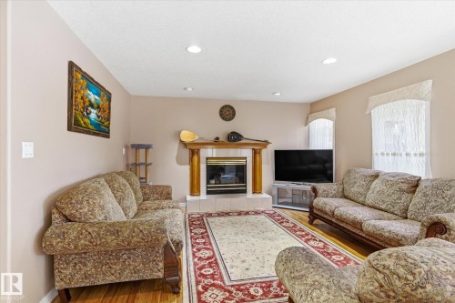 This inviting living area features hardwood flooring, recessed lighting, and a fireplace with a wood mantle - 128 Weaver Drive, Edmonton, AB - Indoor Photo Showing Living Room With Fireplace