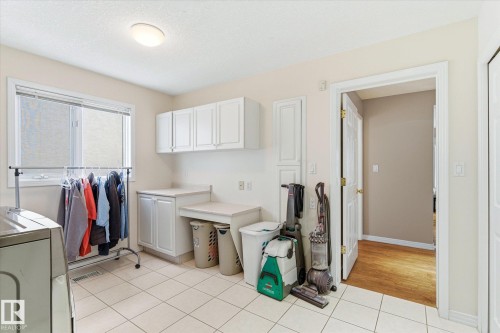 The laundry area features white cabinetry, a window, and tiled flooring - 128 Weaver Drive, Edmonton, AB - Indoor Photo Showing Laundry Room