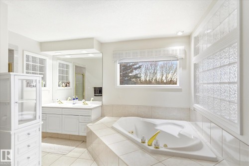 The bathroom features an expansive corner tub, a double vanity with two sinks, and a large mirror - 128 Weaver Drive, Edmonton, AB - Indoor Photo Showing Bathroom