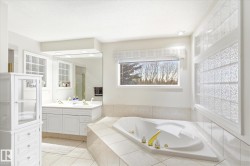 The bathroom features an expansive corner tub, a double vanity with two sinks, and a large mirror - 