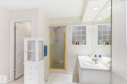 Bathroom featuring a double vanity with white countertops, a glass-enclosed shower, and tiled flooring - 