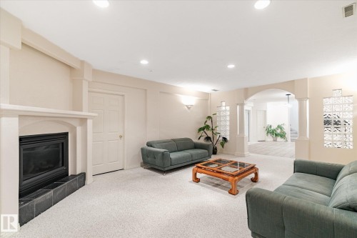 Spacious room featuring light-colored carpeting, a fireplace with a dark tile hearth, and an arched doorway leading to an additional area - 128 Weaver Drive, Edmonton, AB - Indoor Photo Showing Living Room With Fireplace