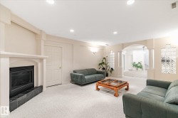 Spacious room featuring light-colored carpeting, a fireplace with a dark tile hearth, and an arched doorway leading to an additional area - 