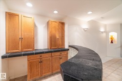 This space features wood cabinetry with dark countertops, a curved stone bar, and recessed lighting - 
