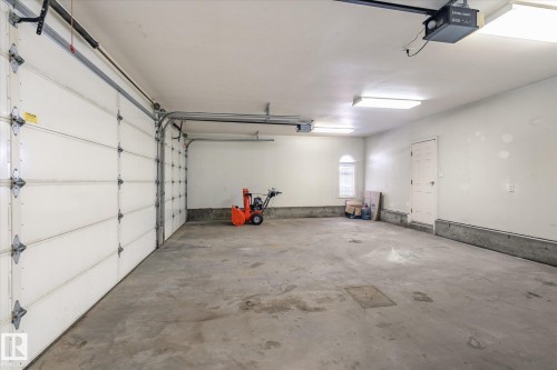 The property features a spacious garage with two overhead doors, a concrete floor, and an arched window providing natural light - 128 Weaver Drive, Edmonton, AB - Indoor Photo Showing Garage