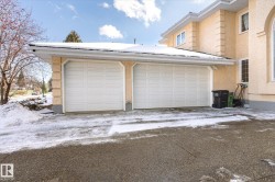 The property features a two-car garage with white paneled doors, set against a light-colored exterior with decorative architectural elements - 