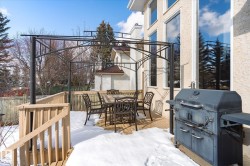 The property features a spacious wooden deck with a black metal pergola structure, offering an outdoor dining area - 