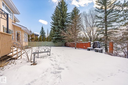 The property features an extensive yard with a snow-covered lawn, mature evergreen trees, and a brick retaining wall - 128 Weaver Drive, Edmonton, AB - Outdoor