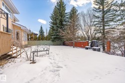 The property features an extensive yard with a snow-covered lawn, mature evergreen trees, and a brick retaining wall - 