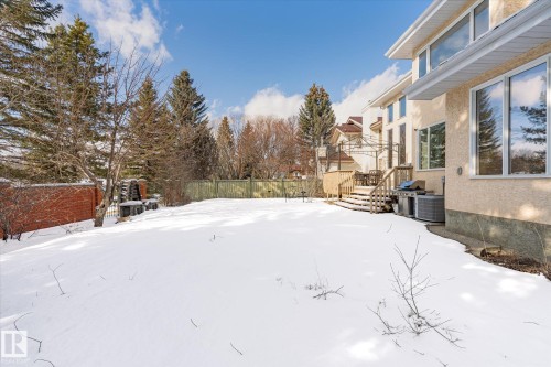 The property features a spacious backyard with a wooden deck and a stucco exterior, set against a backdrop of mature trees - 128 Weaver Drive, Edmonton, AB - Outdoor