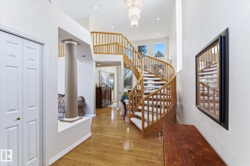 Welcoming entryway featuring a prominent spiral staircase with wood banisters, hardwood flooring, and a decorative chandelier - 128 Weaver Drive, Edmonton, AB - Indoor Photo Showing Other Room