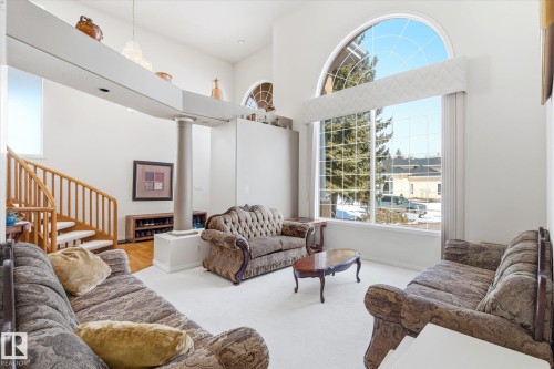 The living area features high ceilings, a grand arched window, and a wooden staircase - 128 Weaver Drive, Edmonton, AB - Indoor Photo Showing Living Room