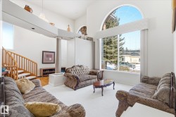The living area features high ceilings, a grand arched window, and a wooden staircase - 
