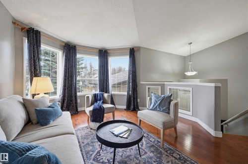 Living area featuring a curved bay window with multiple panes, hardwood flooring, and a decorative pendant light fixture - 21 Escada Close, St. Albert, AB - Indoor Photo Showing Living Room