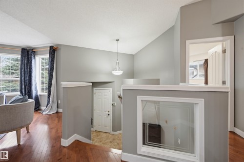 Interior architectural details featuring a multi-level layout, hardwood-finish flooring, a contemporary pendant light fixture, and interior window cutouts - 21 Escada Close, St. Albert, AB - Indoor