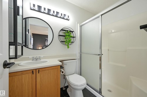 Bathroom featuring a natural wood-finish vanity with an integrated sink, a rectangular vanity light fixture, and a framed circular mirror - 21 Escada Close, St. Albert, AB - Indoor Photo Showing Bathroom