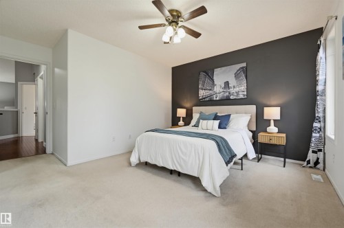 Carpeted bedroom featuring a dark accent wall, a multi-light ceiling fan, and an open doorway revealing wood-finish flooring - 21 Escada Close, St. Albert, AB - Indoor Photo Showing Bedroom