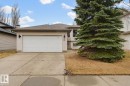 Front exterior featuring light-toned siding, an attached garage with a white door, a paved driveway, and a mature evergreen tree - 21 Escada Close, St. Albert, AB  - Outdoor 