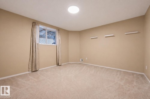 Carpeted room featuring a white window frame, light beige walls, white baseboards, and a circular ceiling light fixture - 21 Escada Close, St. Albert, AB - Indoor Photo Showing Other Room