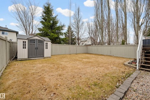 Spacious backyard featuring a two-tone storage shed with double doors, wood privacy fencing, and a multi-level deck with white railings - 21 Escada Close, St. Albert, AB - Outdoor