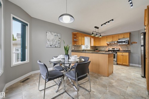 Open-concept kitchen and dining area featuring light wood cabinetry, stone-finish countertops, stainless steel appliances, and large format tile flooring - 21 Escada Close, St. Albert, AB - Indoor