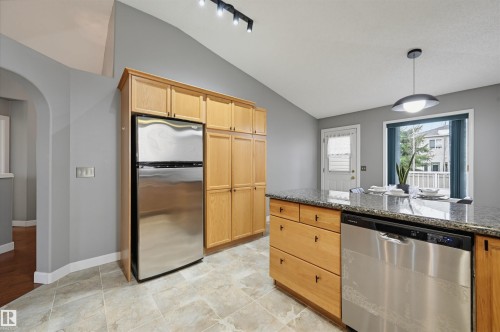 Kitchen featuring a stainless steel refrigerator, light wood cabinetry, a central island with a stone countertop, and tile flooring - 21 Escada Close, St. Albert, AB - Indoor Photo Showing Kitchen
