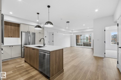 Modern kitchen with a central island featuring a stainless steel sink, integrated dishwasher, and pendant lighting - 202 7459 May Common, Edmonton, AB - Indoor Photo Showing Kitchen With Upgraded Kitchen