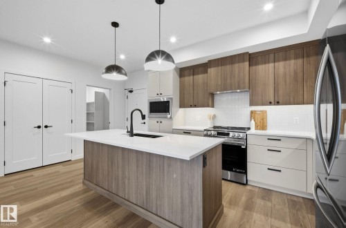 Kitchen featuring a central island with a sink, wood-finish flooring, white countertops, two-tone cabinetry, and stainless steel appliances - 202 7459 May Common, Edmonton, AB - Indoor Photo Showing Kitchen With Upgraded Kitchen