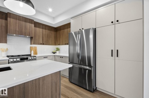 Contemporary kitchen featuring a large island with white stone countertops, wood-finish flooring, and integrated stainless steel appliances - 202 7459 May Common, Edmonton, AB - Indoor Photo Showing Kitchen