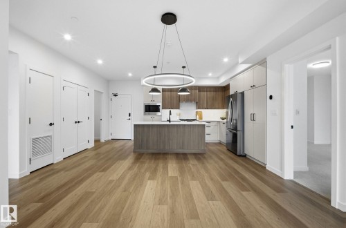 Open-concept living area featuring wood-finish flooring, a kitchen island with seating, pendant lighting, recessed ceiling lights, and contemporary cabinetry - 202 7459 May Common, Edmonton, AB - Indoor Photo Showing Kitchen