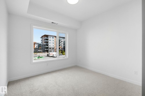 Bright interior space featuring a large window, light-colored carpeting, white walls, and a ceiling-mounted light fixture - 202 7459 May Common, Edmonton, AB - Indoor Photo Showing Other Room