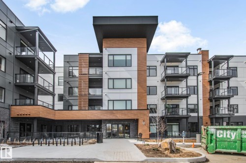 Contemporary multi-story building featuring a prominent central entrance and a mix of exterior finishes - 202 7459 May Common, Edmonton, AB - Outdoor With Balcony With Facade