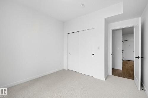 Carpeted room featuring a double-door closet with black hardware - 202 7459 May Common, Edmonton, AB - Indoor Photo Showing Other Room