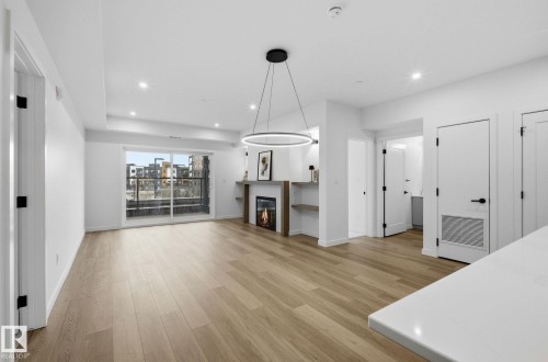 Open-concept living area featuring light wood-finish flooring, a modern fireplace with integrated shelving, and recessed lighting - 202 7459 May Common, Edmonton, AB - Indoor Photo Showing Living Room