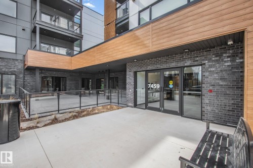 Modern multi-story building entrance featuring dark brick and light wood-finish siding - 202 7459 May Common, Edmonton, AB - Outdoor With Balcony With Exterior