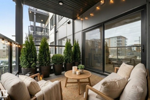 Private balcony with dark soffit, black railings, and sliding glass doors. Virtually staged. - 202 7459 May Common, Edmonton, AB - Outdoor With Deck Patio Veranda With Exterior