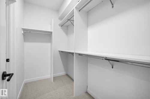 Walk-in closet featuring light-colored carpeting, white shelving, and chrome hanging rods - 202 7459 May Common, Edmonton, AB - Indoor With Storage