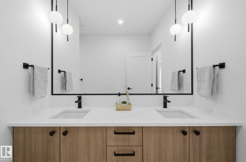 Double vanity with wood-finish cabinetry, integrated sinks, matte black hardware, and a large framed mirror - 202 7459 May Common, Edmonton, AB - Indoor Photo Showing Bathroom