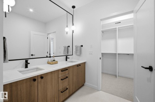 Bathroom vanity featuring a wood-finish double cabinet, dual undermount sinks, and matte black fixtures - 202 7459 May Common, Edmonton, AB - Indoor Photo Showing Bathroom