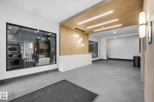 Lobby entry featuring large format grey tile flooring, a wood-paneled ceiling with recessed lighting, and a prominent glass partition - 202 7459 May Common, Edmonton, AB - Indoor Photo Showing Other Room