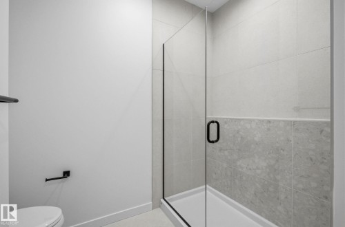 Glass-enclosed shower with matte black hardware, light gray subway tile, and a contrasting light gray stone-finish tile accent - 202 7459 May Common, Edmonton, AB - Indoor Photo Showing Bathroom