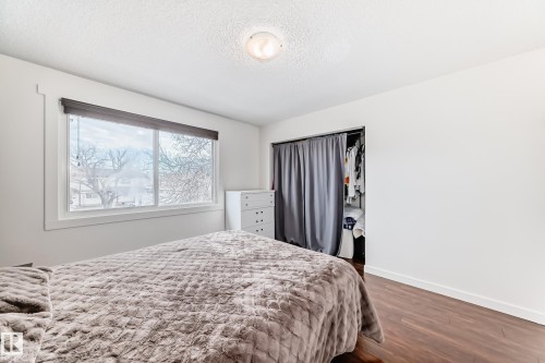 Bright room featuring a large window, dark-finish roller blind, wood-finish flooring, and a recessed closet with privacy curtain - 75 Amberly Court, Edmonton, AB - Indoor Photo Showing Bedroom