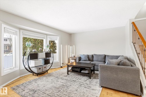 Spacious living area featuring bay windows, parquet wood flooring, painted neutral walls, and a staircase with a wood handrail and metal spindles - 70 Stirling Road, Edmonton, AB - Indoor Photo Showing Living Room