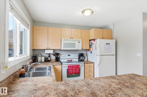 Kitchen featuring light wood-finish cabinetry, a double basin stainless steel sink, and a window with blinds - 70 Stirling Road, Edmonton, AB - Indoor Photo Showing Kitchen With Double Sink