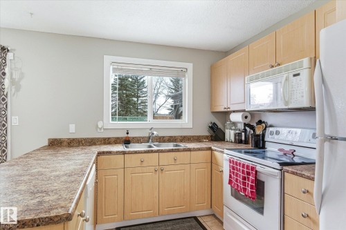 Functional kitchen featuring wood-finish cabinetry, a double basin stainless steel sink, a built-in microwave, an electric range, and a refrigerator - 70 Stirling Road, Edmonton, AB - Indoor Photo Showing Kitchen With Double Sink