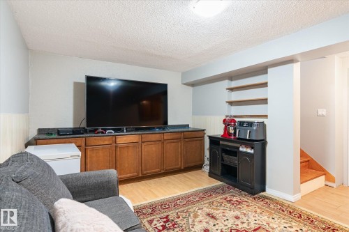 Entertainment area featuring a large built-in media console with wood-finish cabinetry, a dark countertop, and light wood-finish flooring - 70 Stirling Road, Edmonton, AB - Indoor