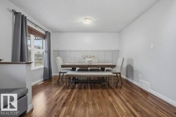 Dining area featuring rich wood-finish flooring, wainscoting detail, a large window with white trim, and a flush-mount ceiling light fixture - 